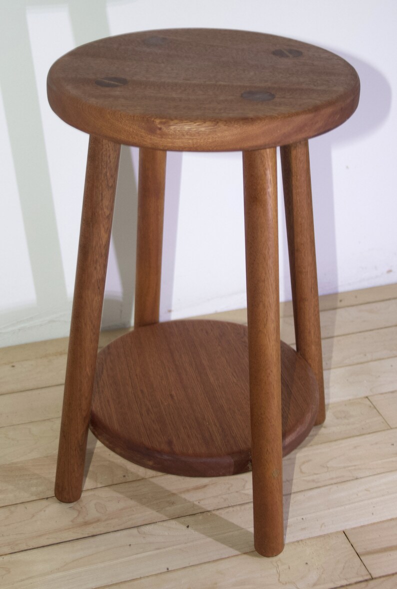May include: A wooden stool with a round top and a lower shelf. The stool is made of dark brown wood and has three legs.