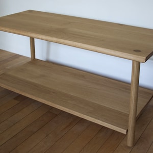 May include: A light wood table with a shelf. The table has a simple design with straight legs and a rectangular top.