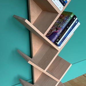May include: A wooden bookshelf shaped like a tree with multiple shelves. The shelves are filled with books with titles like "Journey of Souls", "Earth Magic", and "The Goddess Path".