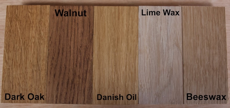 May include: Five rectangular wood samples arranged side-by-side, each displaying a different finish. The labels are Dark Oak, Walnut, Danish Oil, Lime Wax, and Beeswax. Each piece shows distinct wood grain patterns and varying shades of brown.