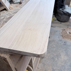 May include: A rectangular light-coloured wooden board with a smooth, sanded surface and rounded corners. The wood grain is visible across the top, showing natural light tan and beige tones in a long, flat, and unfinished plank design.