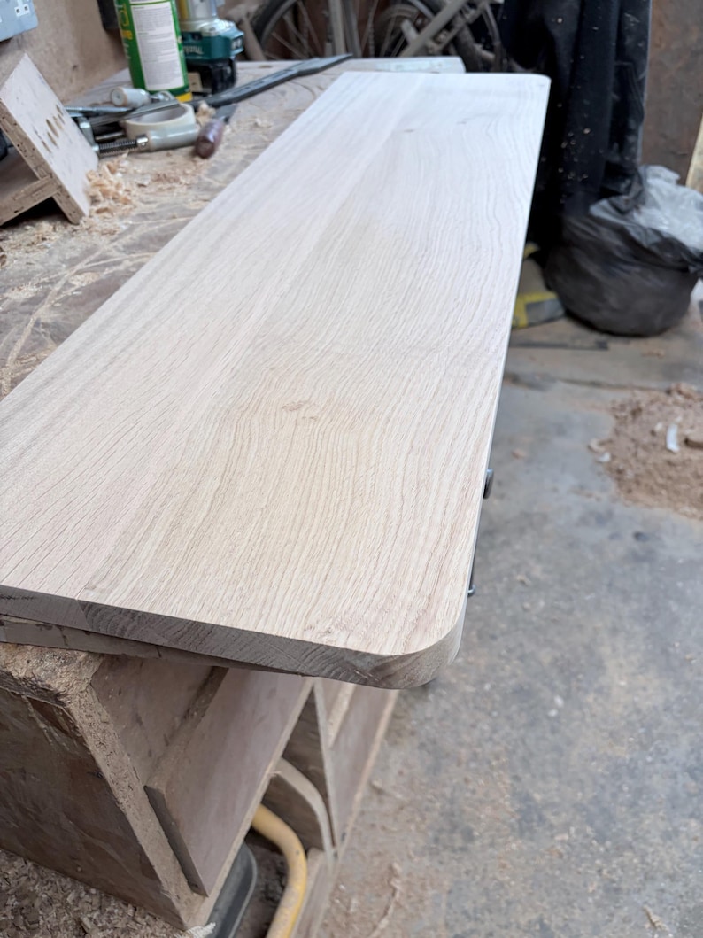 May include: A rectangular light-coloured wooden board with a smooth, sanded surface and rounded corners. The wood grain is visible across the top, showing natural light tan and beige tones in a long, flat, and unfinished plank design.