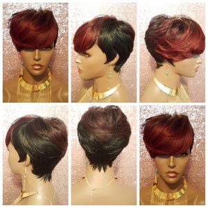 May include: A short, layered wig with a dark brown base and burgundy highlights. The wig is styled in a pixie cut with the top layers styled in a side-swept fringe. The wig is worn on a mannequin head with a gold necklace.