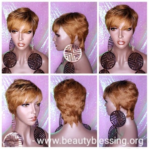 Może przedstawiać: Krótka, warstwowa peruka w kolorze ombre blond i brązowy. Peruka jest ułożona w stylu pixie z grzywką. Perukę nosi manekin z dużymi, okrągłymi kolczykami.