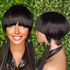 Puede incluir: Una peluca negra corta de estilo bob con flequillo recto. La peluca está peinada con un corte pixie y un acabado liso y recto. La peluca la lleva puesta una modelo con pendientes negros.