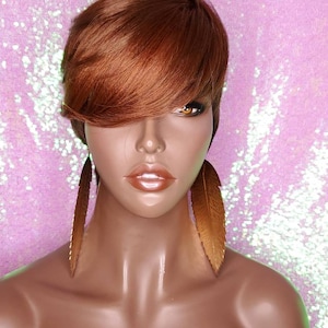May include: A short, choppy, auburn-colored wig with a side part and bangs. The wig is styled with a feathered look and is worn on a mannequin head. The mannequin is wearing long, gold feather earrings.