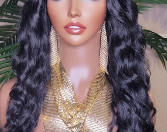 May include: A black wig with loose waves and a straight fringe. The wig is styled on a mannequin head with a gold chain necklace and earrings.