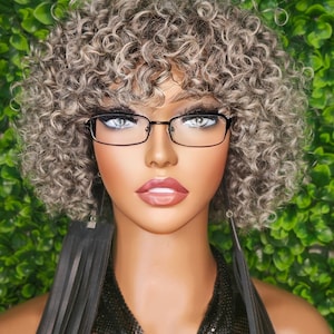 Puede incluir: Un maniquí con el pelo corto, rizado, gris y rubio que lleva gafas con montura negra, un collar de malla negra y pendientes largos de cuero negro.