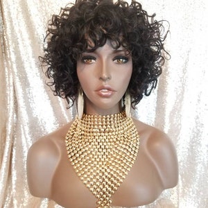 May include: A short, curly, dark brown wig with a side parting. The wig is styled with loose curls and a fringe. The wig is on a mannequin head.