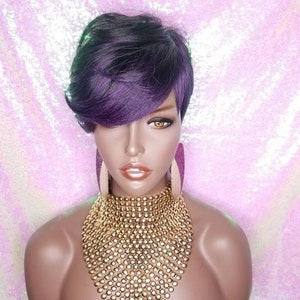 May include: A short, purple and black wig with side-swept bangs. The wig is styled in a pixie cut and is worn on a mannequin head. The mannequin is wearing a gold necklace.