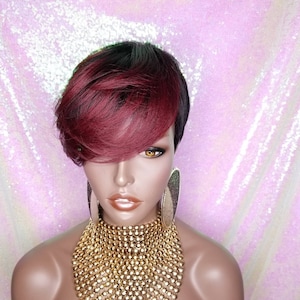 Può includere: Una parrucca corta, liscia e sintetica con una base marrone scuro e riflessi bordeaux. La parrucca è acconciata con una riga laterale e una frangia.