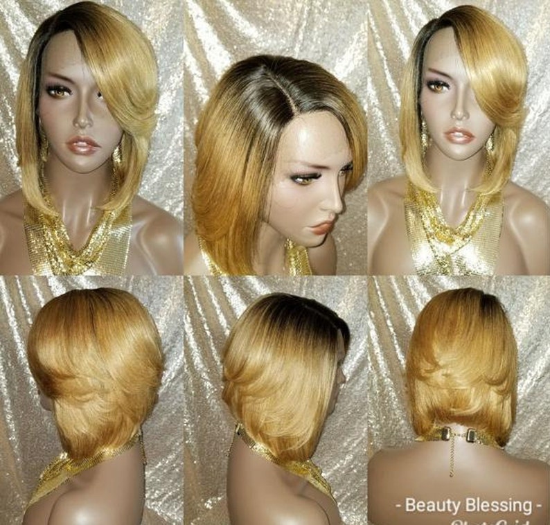 Op de afbeelding: Een kort, recht, blond bob-pruik met donkere wortels. De pruik is gestyled met een scheiding aan de zijkant en een zijwaarts geveegde pony. De pruik wordt gedragen op een mannequinhoofd.
