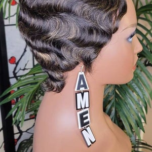 May include: A mannequin with short, wavy, black hair with blonde highlights wearing a pair of long, white earrings that spell out "AMEN" in black letters.