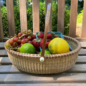 May include: A woven basket with a wooden handle filled with red grapes, strawberries, limes, and a lemon. The basket is sitting on a wooden bench.