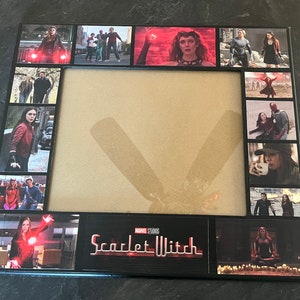 Puede incluir: Un marco de fotos negro con un collage de imágenes de Scarlet Witch del Universo Cinematográfico Marvel. El marco tiene un paspartú marrón y un borde negro. Las imágenes están dispuestas en una cuadrícula y muestran a Scarlet Witch en varias escenas de las películas. El marco también incluye el texto "Scarlet Witch" en una fuente roja y blanca.
