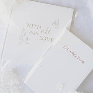 May include: Two white books with gold lettering. The top book says "With all our love" and has a floral design. The bottom book says "little white book".