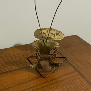 Puede incluir: Una escultura de metal dorado de un insecto con antenas de alambre. El insecto está de pie sobre una base triangular y tiene un letrero que dice "No me molestes".