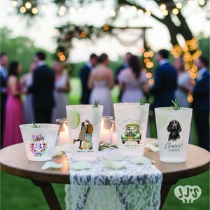 May include: Frosted plastic cups with custom illustrations and text, including a couple, a vintage car, and a dog. The cups are decorated with floral designs and the words "Cheers!" and "Just Married". The cups are on a wooden table with candles and a lace tablecloth.