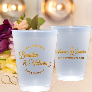 May include: Two white plastic cups with gold lettering. The cup on the left says "Mr. and Mrs. Branden & Victoria URBANOUSKY". The cup on the right says "Victoria & Branden EST. NOVEMBER 20, 2021".