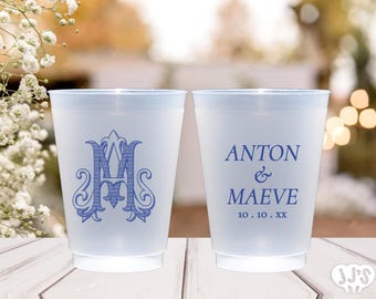 May include: Two frosted plastic cups with a light blue rim. One cup features a blue monogram, the other has the names "ANTON & MAEVE" and a date. Wedding or party theme.