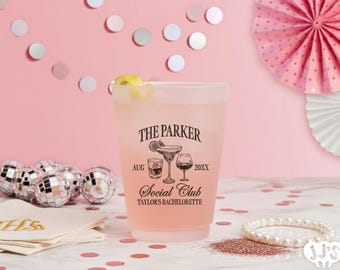 May include: A frosted plastic cup filled with a pink beverage and a lemon garnish. The cup is printed with "THE PARKER Social Club" and "Taylor's Bachelorette". Decorative disco balls, confetti, and a pearl bracelet are also visible.
