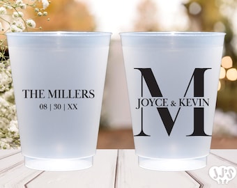 May include: Two frosted plastic cups with black text. One cup reads "THE MILLERS" with a date below. The other cup has a large "M" with "JOYCE & KEVIN" above and below. Wedding or party theme.