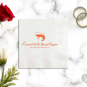 May include: White paper napkin with a red shrimp illustration and the text "I want to be loved bayou" with the names Amy and Chad and the location Houston, TX.
