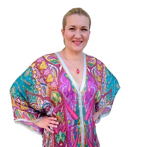 May include: A woman wearing a colorful, patterned tunic with a V-neck and long sleeves. The tunic has a paisley design in shades of pink, teal, yellow, and gold.