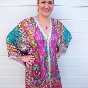 May include: A woman wearing a colorful, patterned tunic with a V-neckline and long sleeves. The tunic has a paisley design in shades of pink, blue, green, and yellow.