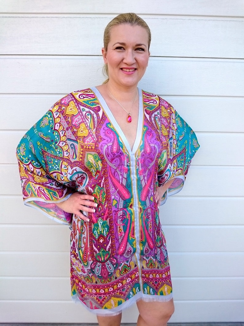 May include: A woman wearing a colorful, patterned tunic with a V-neckline and long sleeves. The tunic has a paisley design in shades of pink, blue, green, and yellow.