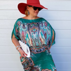 A woman wearing a green and blue paisley patterned maxi dress with a red wide-brimmed hat and a white clutch.
