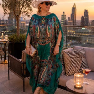 Designer inspired aquamarine silk paisley kaftan in a rooftop restaurant setting, flowing maxi beach cover up and plus size vacation outfit.