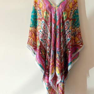 May include: A colorful, patterned, silk kaftan with a V-neckline. The kaftan is a vibrant mix of pink, red, yellow, blue, and white.