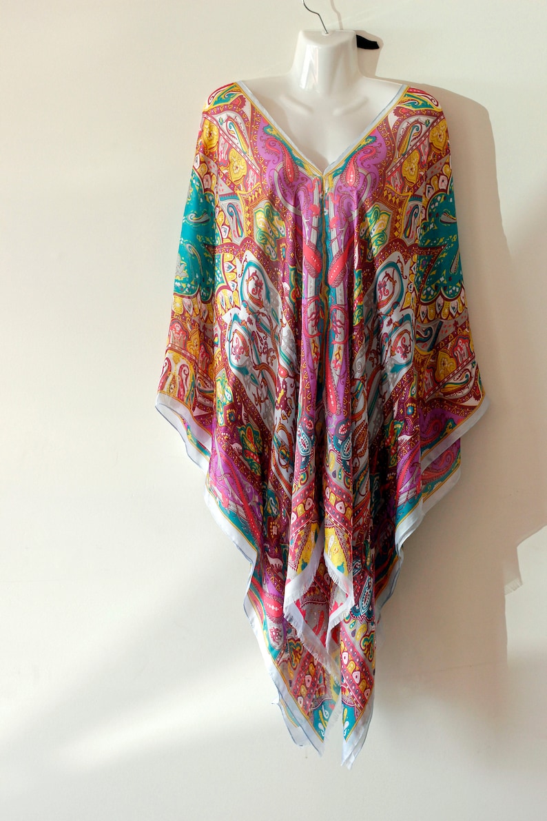 May include: A colorful, patterned, silk kaftan with a V-neckline. The kaftan is a vibrant mix of pink, red, yellow, blue, and white.