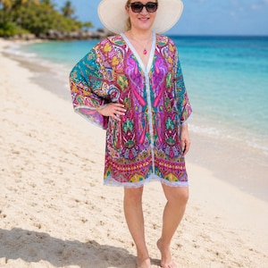 Turquoise pink paisley silk kaftan top worn as a beach cover up with white sun hat on a tropical beach.