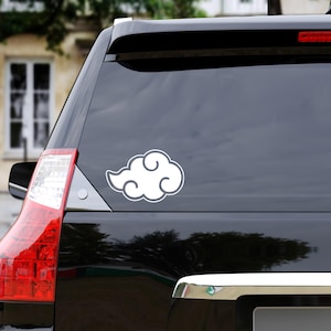 May include: White cloud sticker with a gray outline, affixed to the rear window of a black vehicle. The sticker features a stylized cloud design, commonly seen in anime and manga. The sticker is positioned on the lower right side of the window.