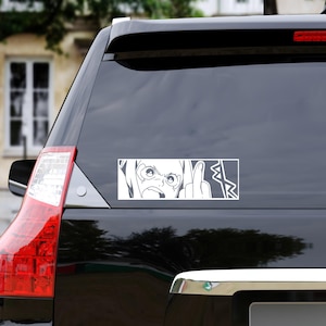 May include: White rectangular car decal featuring a black and white anime-style illustration. The image depicts a person with an angry expression, giving the middle finger. The design includes stylized lines and shapes.
