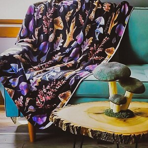 May include: A wooden side table with a live edge top and black hairpin legs. The table is decorated with a cluster of three ceramic mushrooms in shades of brown and white. The table is sitting on a colorful rug.