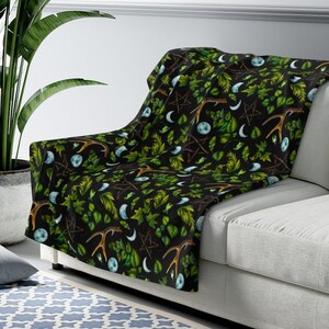 May include: A black throw blanket with a repeating pattern of green leaves, antlers, moons, and pentagrams.