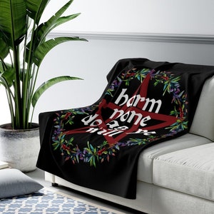 May include: Black fleece throw blanket with a red pentagram and the text "harm none do all be" in white lettering. The pentagram is surrounded by a wreath of green leaves and purple flowers.