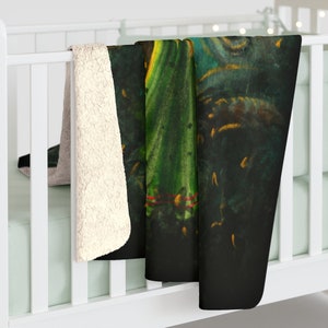 May include: A soft, plush throw blanket with a dark background and a vibrant green and yellow abstract design. The blanket is folded and draped over a white crib.