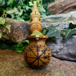 May include: A wooden wand with a carved wooden orb at the end. The orb is decorated with a compass design and runes. The wand is made of light brown wood and has a brass accent.