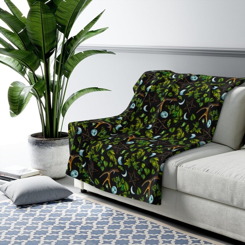 May include: A black throw blanket with a repeating pattern of green leaves, antlers, moons, and pentagrams.