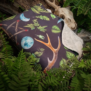 May include: A black and green throw blanket with a nature-inspired design featuring antlers, leaves, moons, and a crystal ball. The blanket has a soft, white fleece lining.