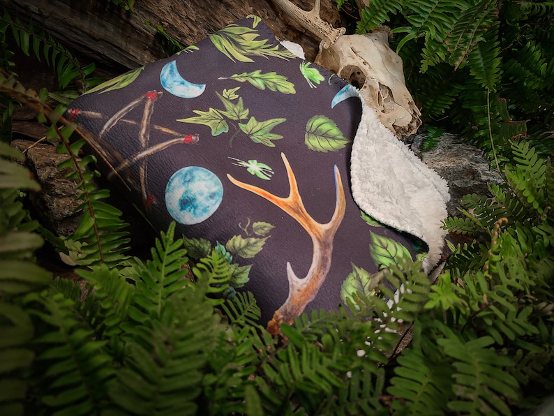May include: A black and green throw blanket with a nature-inspired design featuring antlers, leaves, moons, and a crystal ball. The blanket has a soft, white fleece lining.