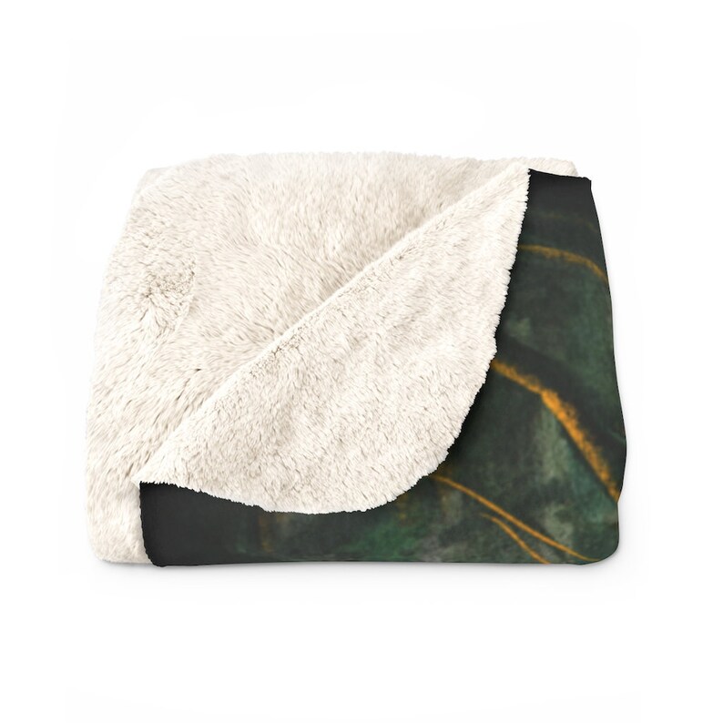 May include: A soft, plush throw blanket with a white sherpa fleece backing and a printed front featuring a dark green and gold abstract design.