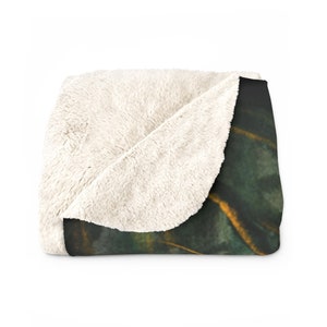 May include: A soft, plush throw blanket with a white sherpa fleece side and a printed side featuring a dark green and gold abstract design.