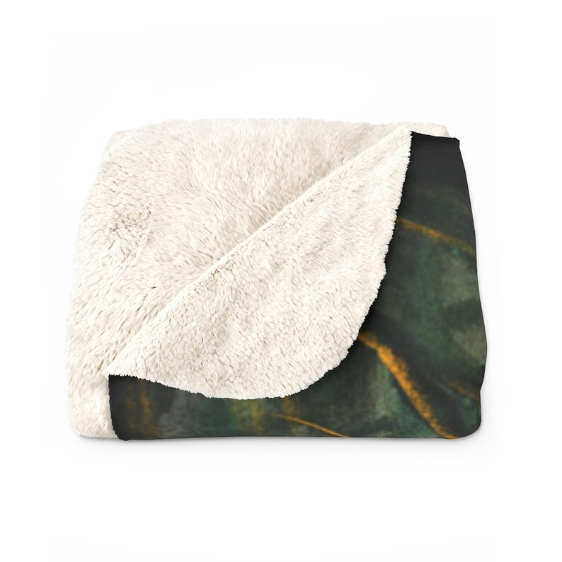 May include: A soft, plush throw blanket with a white sherpa fleece side and a printed side featuring a dark green and gold abstract design.