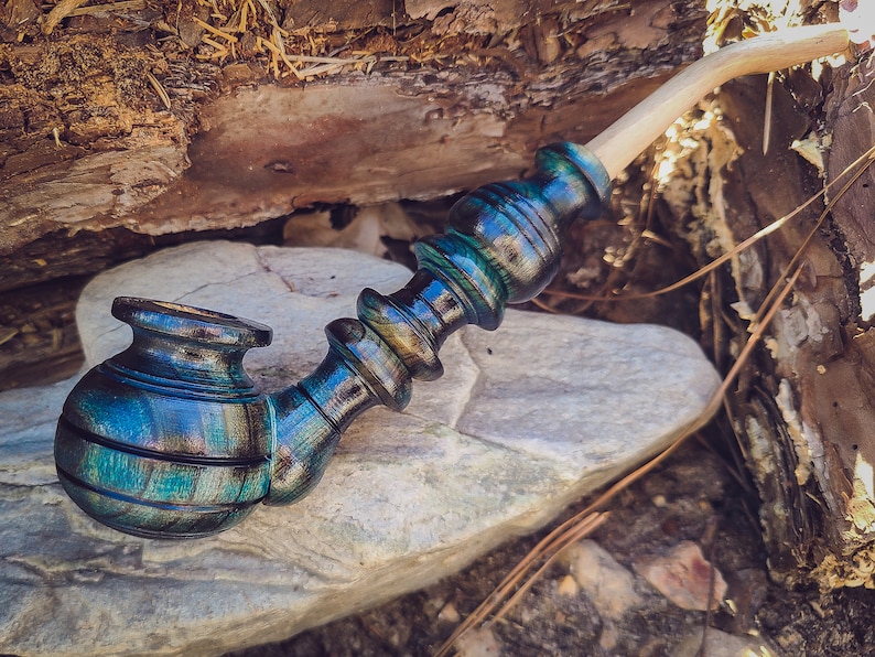 May include: A wooden smoking pipe with a blue, green, and black swirl pattern. The pipe has a long, curved stem and a bowl with a rounded shape.