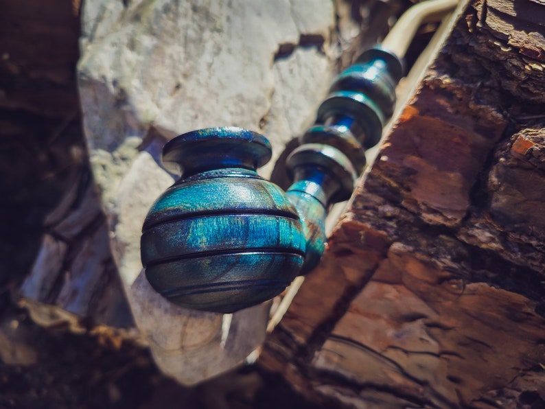 May include: A blue and green wooden pipe with a round bowl. The pipe is resting on a piece of tree bark.